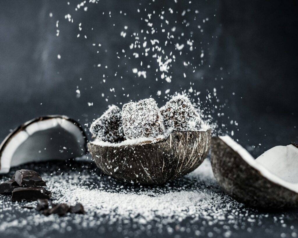 The History of Desiccated Coconut Powder - How it Was Developed, When it Became Popular, and Key Moments in Its Rise as an Ingredient. 1 brown wooden bowl on white snow, desiccated coconut powder, organic desiccated coconut, unsweetened desiccated coconut, desiccated coconut flakes