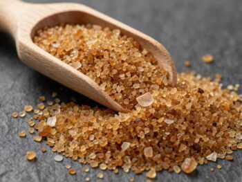 Coconut sugar granules spilling from a wooden scoop.