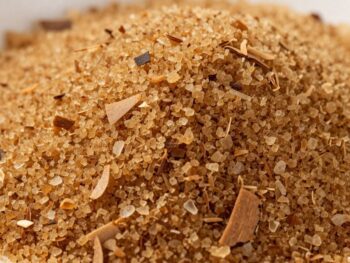 Pile of granular coconut sugar with scattered coconut flakes. {{brizy_dc_image_alt entityId=